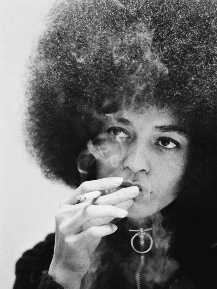 A black-and-white portrait of a woman with an afro, holding a cigarette.