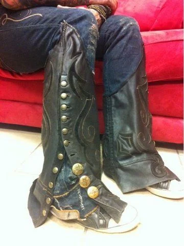 Tall black boots with silver buttons and embroidered details resting beside a red couch.