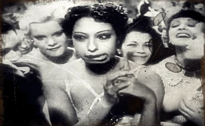 A black-and-white scene with a woman smoking a pipe in a crowd.