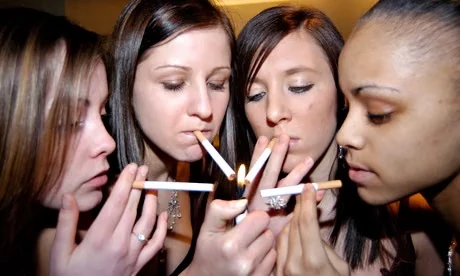 A group gathered closely together, holding cigarettes.