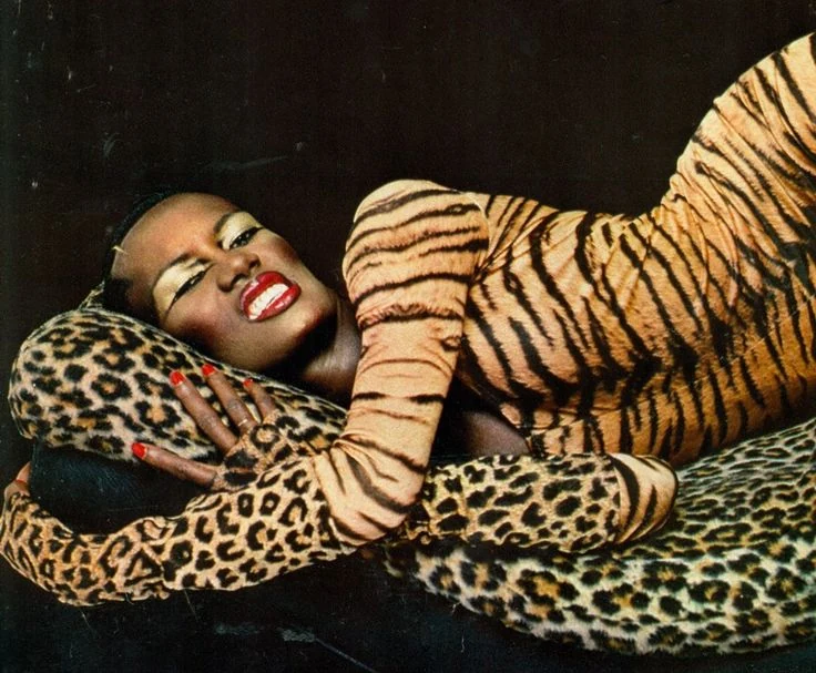 A reclining figure wearing tiger stripes against a leopard-patterned chair.