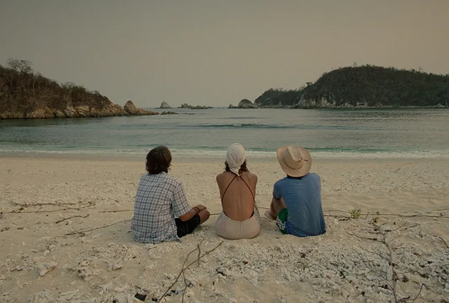 Three friends sitting together on the beach in Y tu mamá también.